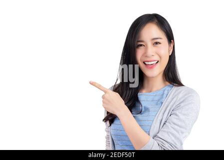 Belle femme asiatique confiante dans des vêtements décontractés souriant et pointant de la main vers l'espace vide de côté, studio tourné isolé sur fond blanc Banque D'Images
