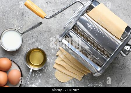 Machine à pâtes avec pâte et ingrédients sur fond gris Banque D'Images