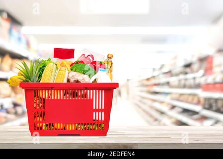 Nourriture et épicerie dans le panier rouge sur table en bois avec une allée de marché en arrière-plan floue Banque D'Images