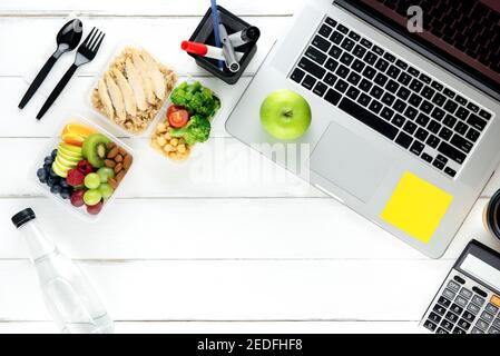 Prêt à manger sain et propre manger des aliments à faible teneur en gras dans une boîte à repas préparée pour le déjeuner sur une table de travail avec ordinateur portable et fournitures de bureau, vue du dessus Banque D'Images