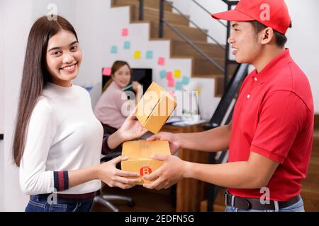 Livrant le colis au propriétaire. Femme acceptant une livraison de boîtes de livreur. Le liveur porte un uniforme rouge envoyé à l'emballage de la boîte Banque D'Images