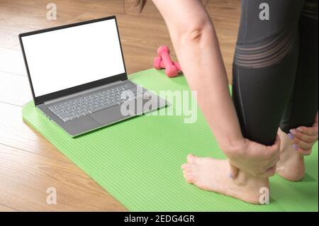 Gros plan des pieds et des paumes féminins sur le tapis de yoga avec ordinateur portable. Personnes pratiquant le yoga en ligne. Concept de cours de formation vidéo sur les appareils numériques. Flexible Banque D'Images