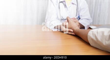 Médecin travaillant dans sa clinique et à l'écoute du patient, le docteur tient la main du patient et à l'écoute expliquant ses symptômes Banque D'Images