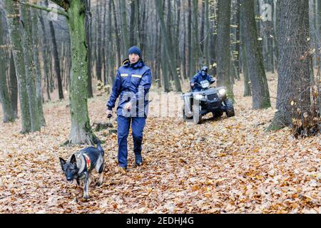 Un secouriste avec un chien sur une laisse recherche dans les bois, un sauveteur sur un ATV recherche également. Recherchez un homme dans les bois Banque D'Images