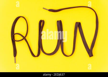 Mot « run » fait de lacets athlétiques marron sur fond jaune. Composition créative de la pose à plat. Banque D'Images