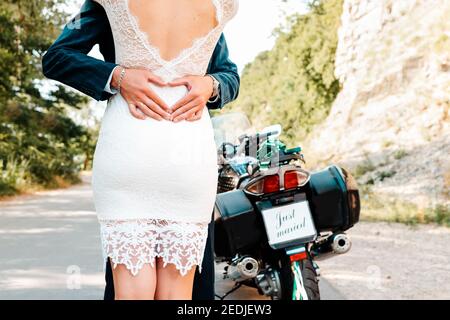 Mariage, jeunes mariés. Des hugs d'un homme et d'une femme dans des robes de mariage. Il y a une moto en arrière-plan. Été. Extérieur. Vue arrière. Gros plan. Banque D'Images