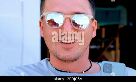 Positif jeune homme portant des lunettes de soleil miroir stylées souriant à attrayant femme réfléchissant dans des verres sur la plage de la mer vue proche Banque D'Images