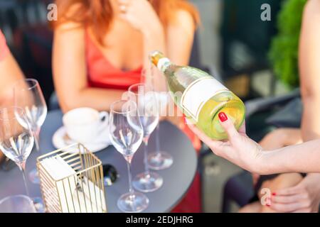 Un serveur femme de gros plan qui tient une bouteille de champagne blanc ou un prosecco à l'extérieur le jour d'été lumineux. Concept de fête des filles. Vie de luxe Banque D'Images