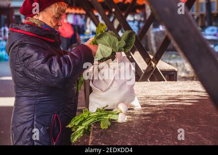 La femme âgée met les légumes achetés sur le marché dans un sac en tissu, un mode de vie sain Banque D'Images