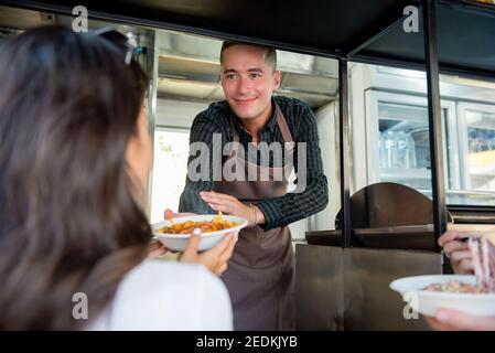 Un serveur sur un camion alimentaire donne des pâtes dans une assiette à emporter à femme cliente Banque D'Images