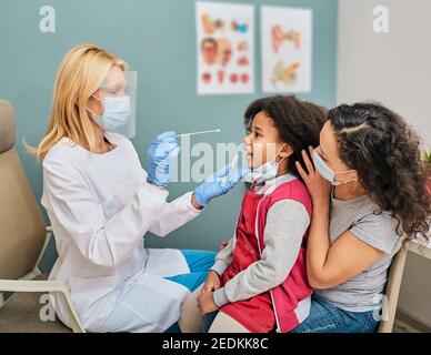 Petite fille avec son parent pendant le test PCR de Covid-19 dans une clinique médicale. Écouvillon oral pour le prélèvement d'échantillons de coronavirus Banque D'Images