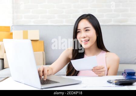 Jeune femme asiatique entrepreneur ou freelance vendeur en ligne travaillant sur ordinateur portable vérifier la commande sur internet à la maison se préparer pour livraison Banque D'Images