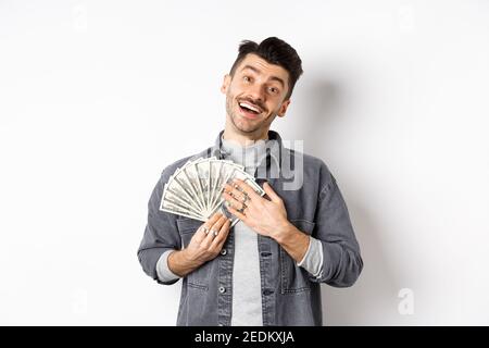 Un homme souriant qui fait de l'argent, enserre des billets de dollars avec un visage soulagé heureux, debout sur fond blanc Banque D'Images