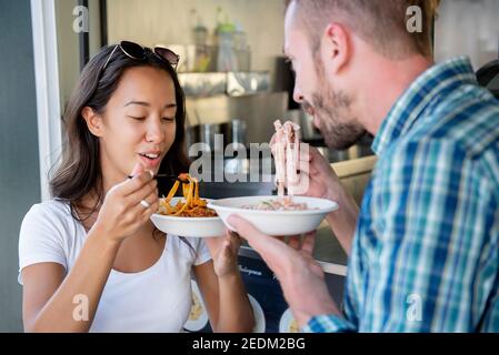 Jeune couple interracial appréciant manger des pâtes du camion alimentaire Banque D'Images