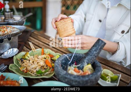 Femme ouvrant le récipient de bambou de riz collant tout en ayant un trois Repas dans un restaurant thaïlandais à proximité Banque D'Images