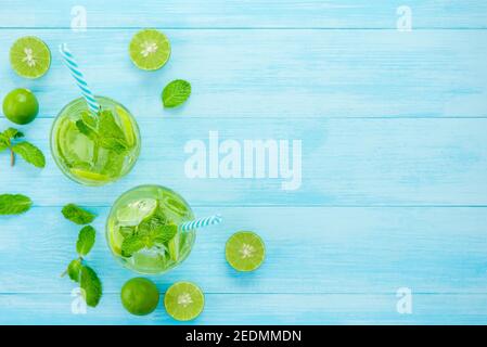 Des cocktails Mojito rafraîchissants dans les verres avec des limes et des feuilles de menthe sur fond de table en bois bleu clair, vue du dessus avec espace pour les copies Banque D'Images