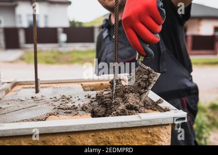 Un constructeur de briques applique une solution adhésive pour poser un rangée de briques et de blocs sur un mur Banque D'Images