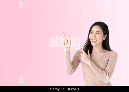 Belle jeune femme asiatique décontractée souriant et pointant les mains vers l'espace vide de côté, studio tourné sur fond rose Banque D'Images