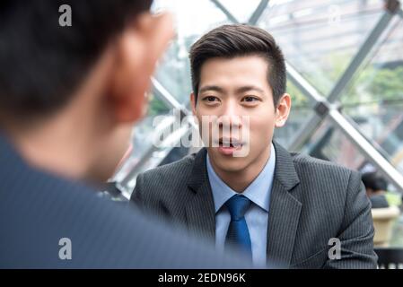 Un jeune homme d'affaires asiatique charmant qui parle avec son partenaire contact visuel au salon du bureau Banque D'Images