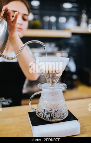 La fille prépare du café à travers un filtre dans un goutte-à-goutte et la verse dans une tasse en verre Banque D'Images