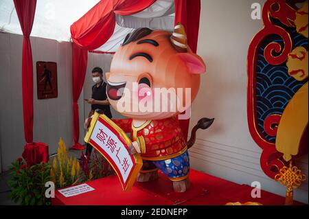 29.01.2021, Singapour, , Singapour - UN homme portant un masque de visage marche devant une figurine décorative liée au signe du zodiaque chinois du boeuf en face Banque D'Images