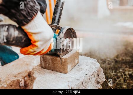 Bricklayer coupe la pierre à l'aide d'une meuleuse angulaire - rapide et sûre - poussière des outils électriques Banque D'Images