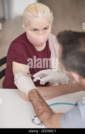 Portrait d'un médecin méconnaissable qui vaccine une femme âgée portant un masque contre covid 19 Banque D'Images