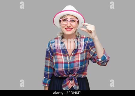 J'ai besoin d'un peu plus. Portrait de femme mature chic et moderne avec plaisir dans un style décontracté avec chapeau et lunettes debout et demande quelque chose de plus. Banque D'Images