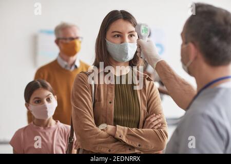 Prise de vue d'un médecin méconnaissable vérifiant la température d'une jeune femme portant un masque et attendant dans la file d'attente à la clinique ou à l'hôpital, espace de copie Banque D'Images