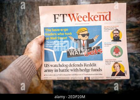 Londres, Royaume-Uni - 2 févr. 2021: POV main mâle tenant Financial Times FT week-end journal lisant sur les transactions de Paris de Wall Street sur un forum Reddit Banque D'Images