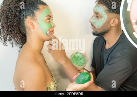 Homme appliquant le masque d'avocat sur le visage de sa petite amie. Jeune couple prenant soin de la peau à la maison. Concept santé et spa. Banque D'Images