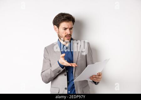 Un employeur en colère qui regarde un mauvais document, se plaint d'une affaire, fait remarquer que le papier est frustré, se tenant en procès sur fond blanc Banque D'Images