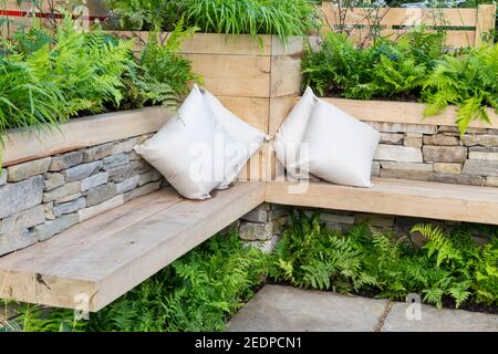 Un banc en bois avec des coussins dans un coin salon Et des lits en pierre sèche avec fougères et Hosta Plantes poussant Angleterre GB Royaume-Uni Banque D'Images