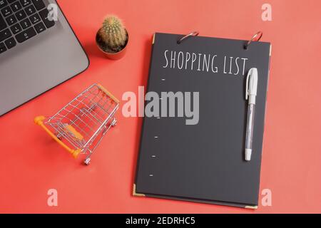 Liste d'achats écrite sur papier noir. Concept de la liste de contrôle alimentaire. Copier l'espace. Isolé sur fond rouge. À côté de la liste se trouve le mini panier. Banque D'Images