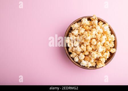 Pop-corn au caramel dans un bol en bois sur fond rose pastel. Vue de dessus, plat, espace de copie. Banque D'Images