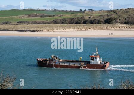 Bateau de dragage à basse altitude rouge quittant le port de Padstow tout en pompant l'excès d'eau des bilges. Scène lumineuse. Banque D'Images