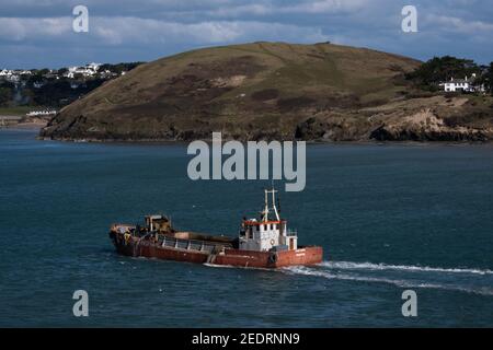 Bateau de dragage à basse altitude rouge quittant le port de Padstow tout en pompant l'excès d'eau des bilges. Scène lumineuse. Banque D'Images