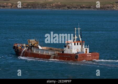 Bateau de dragage à basse altitude rouge quittant le port de Padstow tout en pompant l'excès d'eau des bilges. Scène lumineuse. Banque D'Images