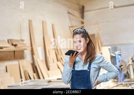 Jeune femme artisan parlant au téléphone avec un smartphone atelier de menuiserie Banque D'Images