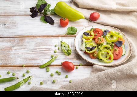 Salade végétarienne de pois verts, tomates, poivre et basilic sur fond blanc en bois et linge de maison. Vue latérale, espace de copie. Banque D'Images