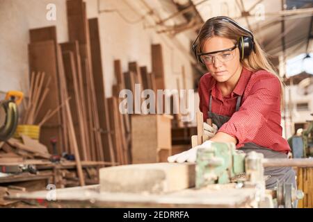 Femme en tant que stagiaire en charpentier plantant du bois avec une main avion avec protection auditive Banque D'Images