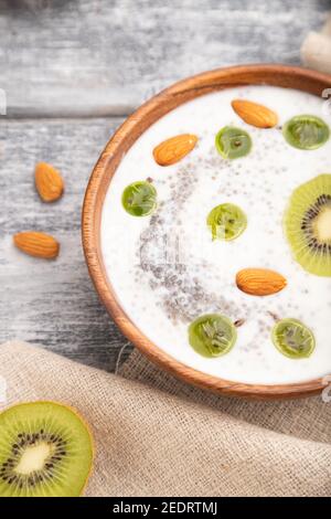 Yaourt au kiwi, à la groseille, au chia et aux amandes dans un bol en bois sur fond en bois gris et linge de maison. Vue latérale, gros plan, mise au point sélective. Banque D'Images