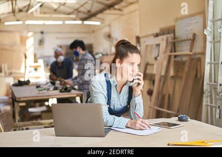 Femme artisan parlant à un client au téléphone un atelier de menuiserie Banque D'Images