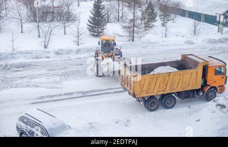 Le gros tracteur jaune nettoie la neige de la route et la charge dans le camion. Nettoyage et nettoyage des routes de la ville de la neige en hiver Banque D'Images