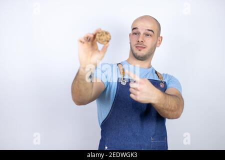Jeune homme bald portant un tablier uniforme sur un fond blanc isolé Jeune homme bald portant un tablier uniforme sur un fond blanc isolé tenir un choc Banque D'Images