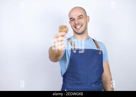 Jeune homme bald portant un tablier uniforme sur un fond blanc isolé Jeune homme bald portant un tablier uniforme sur un fond blanc isolé tenir un choc Banque D'Images