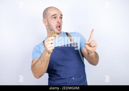 Jeune homme bald portant un tablier uniforme sur un fond blanc isolé Jeune homme bald portant un tablier uniforme sur un fond blanc isolé tenir un choc Banque D'Images