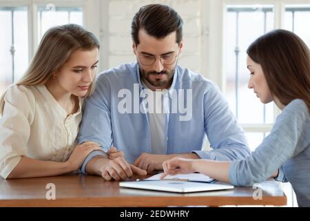 Jeune couple marié et concentré discutant d'un accord avec un courtier qualifié. Banque D'Images