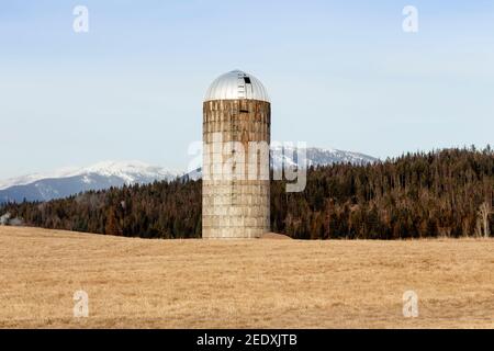 Un vieux silo en béton sur une ferme, près de Iron Creek, à l'extérieur de Troy, Montana. Sommets enneigés de la chaîne de montagnes Cabinet au loin. Banque D'Images