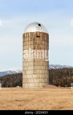 Un vieux silo en béton sur une ferme, près de Iron Creek, à l'extérieur de Troy, Montana. Sommets enneigés de la chaîne de montagnes Cabinet au loin. Banque D'Images